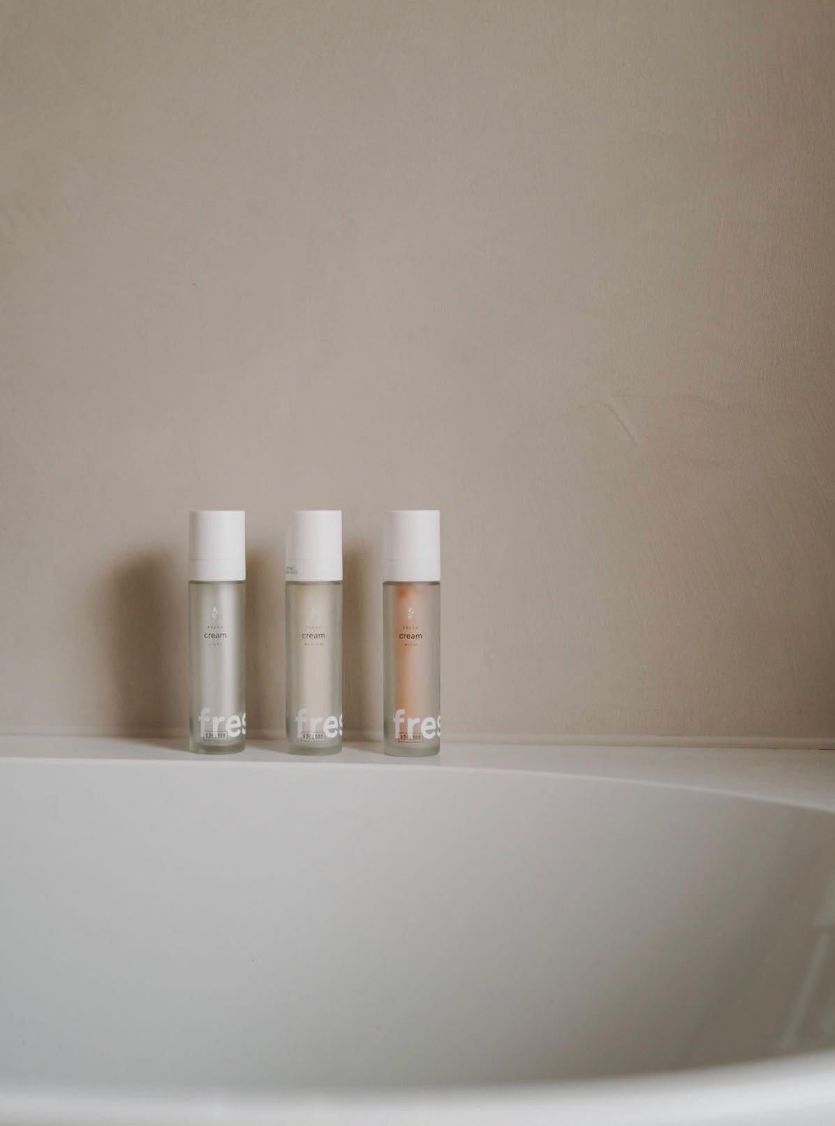 Drei Glasflaschen mit weißen Deckeln auf dem Rand einer hellen Badewanne